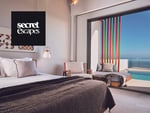 Luxurious hotel room with modern decor, featuring a comfortable bed and large windows showcasing a stunning ocean view. Perfect for a relaxing getaway. Secret Escapes logo in the corner.