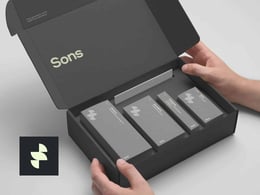 Hands holding an open black box containing four sleek product packages, with the brand name "Sons" prominently displayed on the inside lid. A logo featuring a stylized design is visible in the corner.