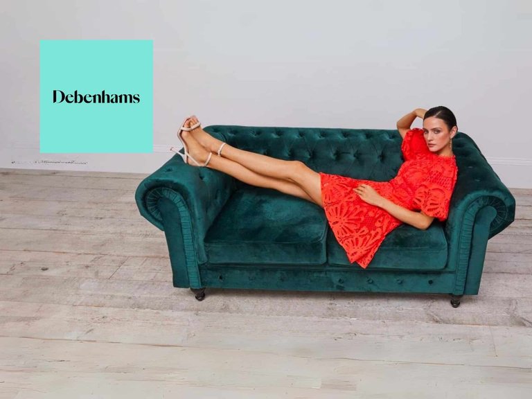 Model In A Red Floral Dress Lounging On A Teal Velvet Couch, Showcasing A Stylish And Modern Interior Design.