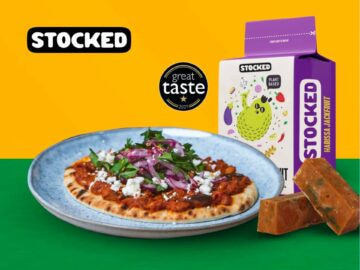 Delicious flatbread topped with savory sauce, fresh herbs, and diced onions, accompanied by a box of STOCKED plant-based seasoning cubes on a vibrant background.