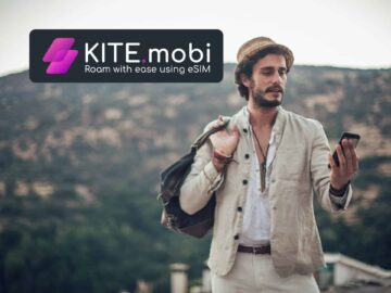 Man in casual attire using a smartphone outdoors with mountains in the background, featuring the KITE.mobi logo promoting mobile power solutions.