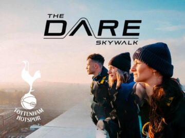Three individuals stand on a rooftop, gazing into the distance during the Dare Skywalk experience at Tottenham Hotspur Stadium, showcasing an adventurous outdoor activity with a scenic view.