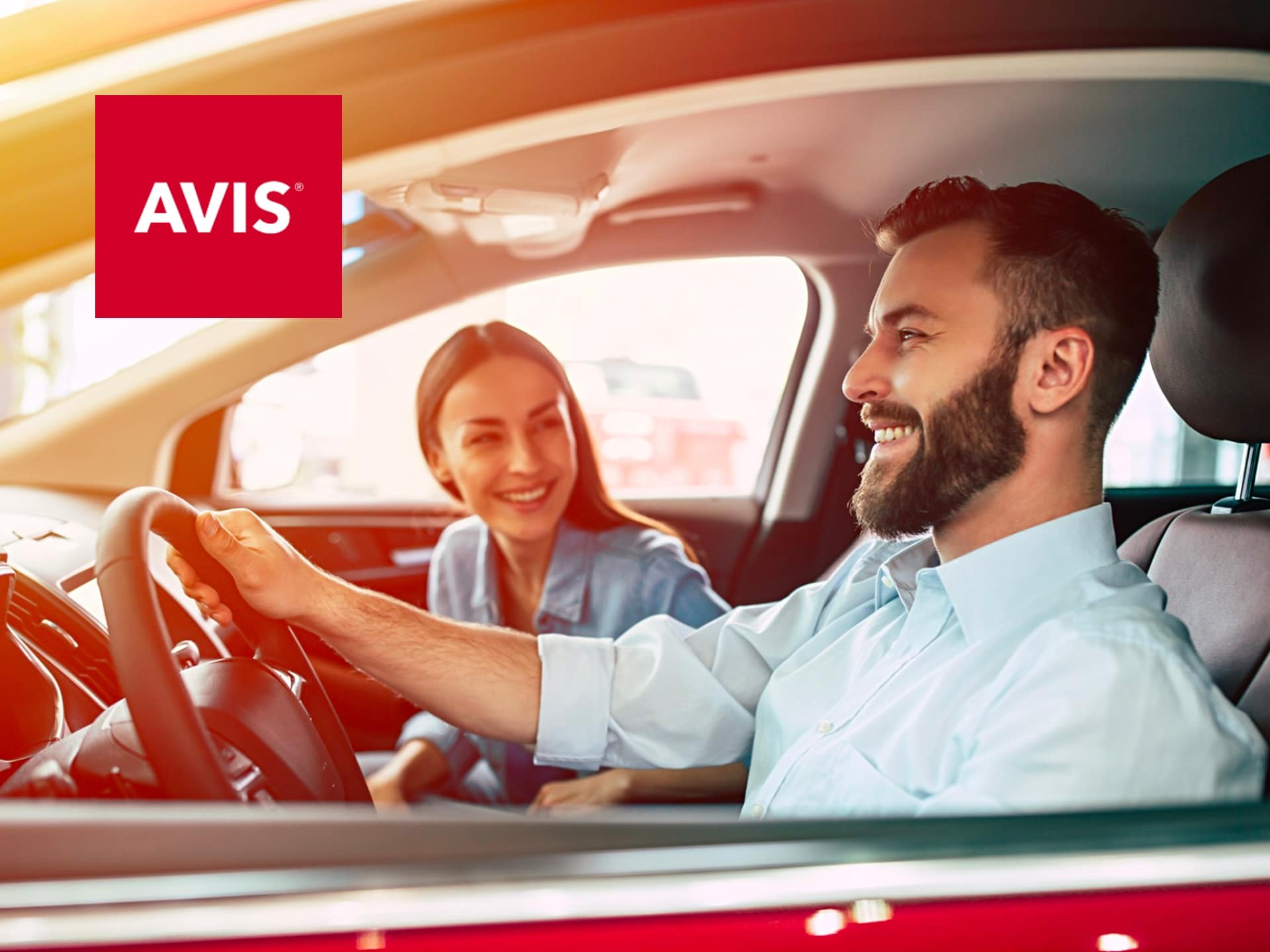 A Smiling Man Driving A Car With A Woman Passenger, Both Enjoying Their Ride, With The Avis Logo Visible In The Corner, Highlighting A Positive Car Rental Experience.