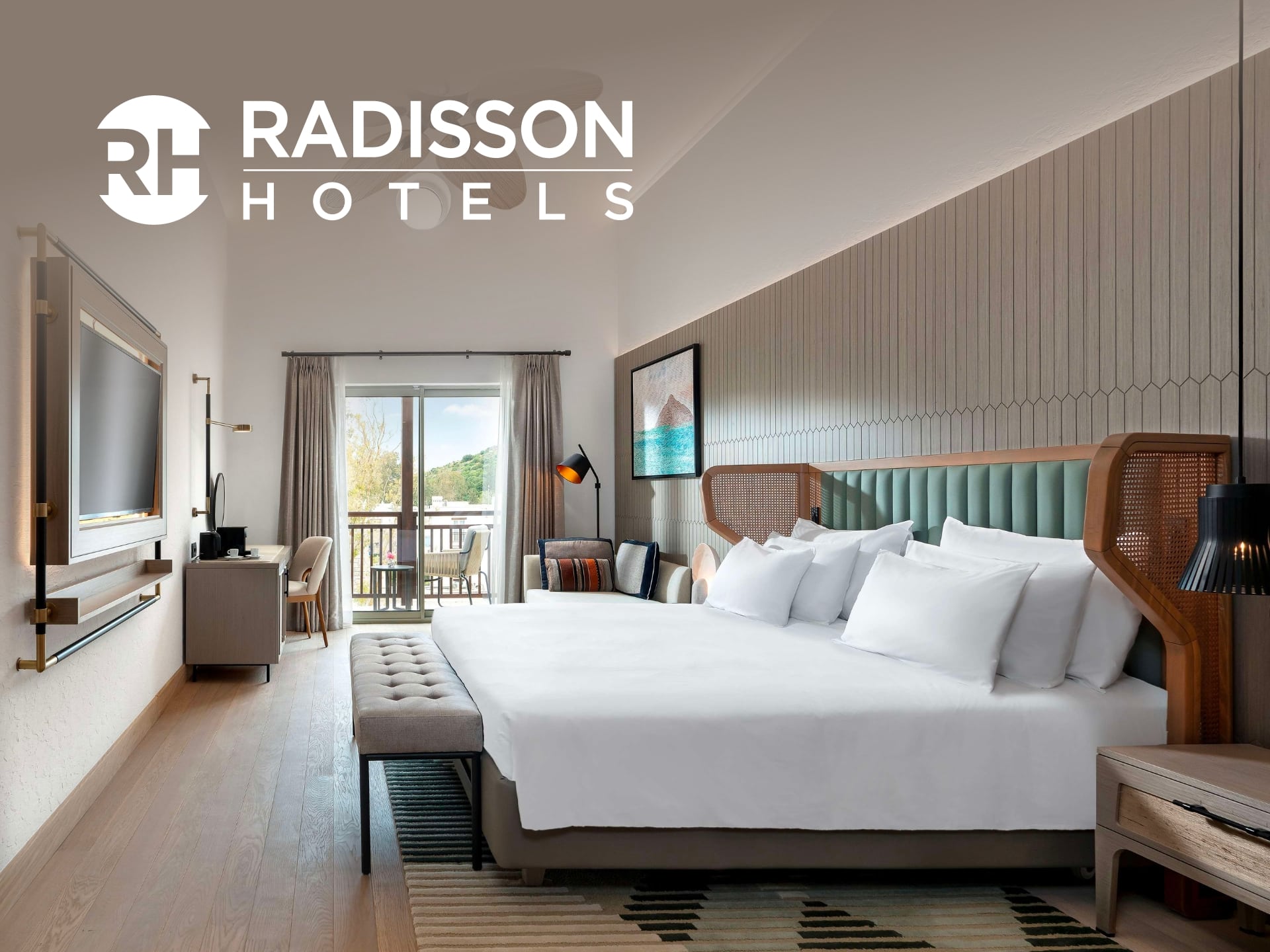 Modern hotel room featuring a spacious layout, large bed with white linens, stylish decor, and natural light streaming in from large windows. Radisson Hotels logo displayed prominently.