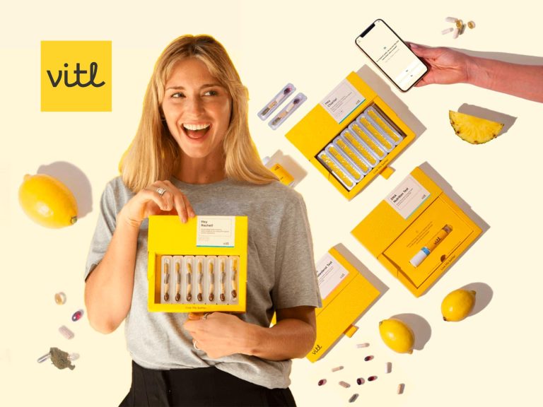 Smiling Woman Holding A Box Of Personalized Vitamins From Vitl, Surrounded By Vitamin Packs And A Smartphone Displaying The Vitl App, Showcasing A Modern Health And Wellness Lifestyle.
