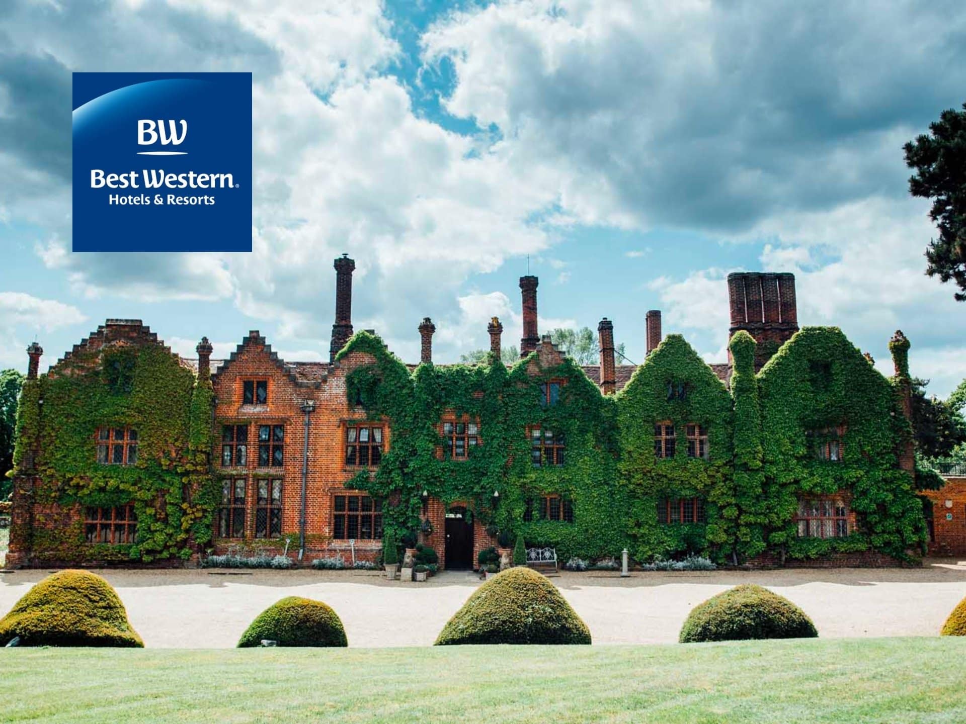 Historic Mansion Covered In Greenery With A Scenic Landscape, Featuring A Blue Logo In The Corner. Ideal For Showcasing Heritage Architecture And Natural Beauty.