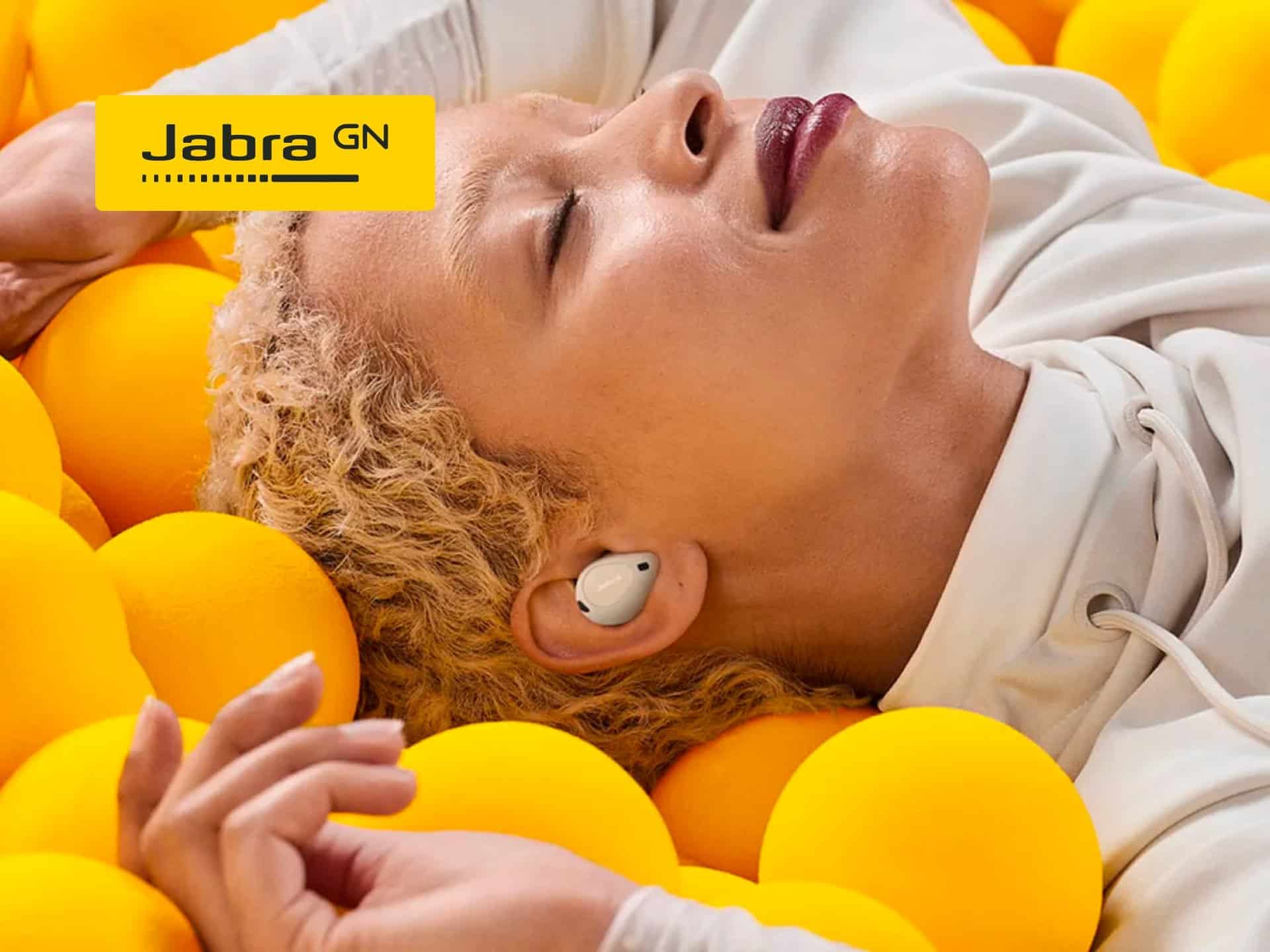 Woman Relaxing Among Yellow Balls While Wearing Jabra Earbuds, Showcasing Comfort And Style In Audio Technology.