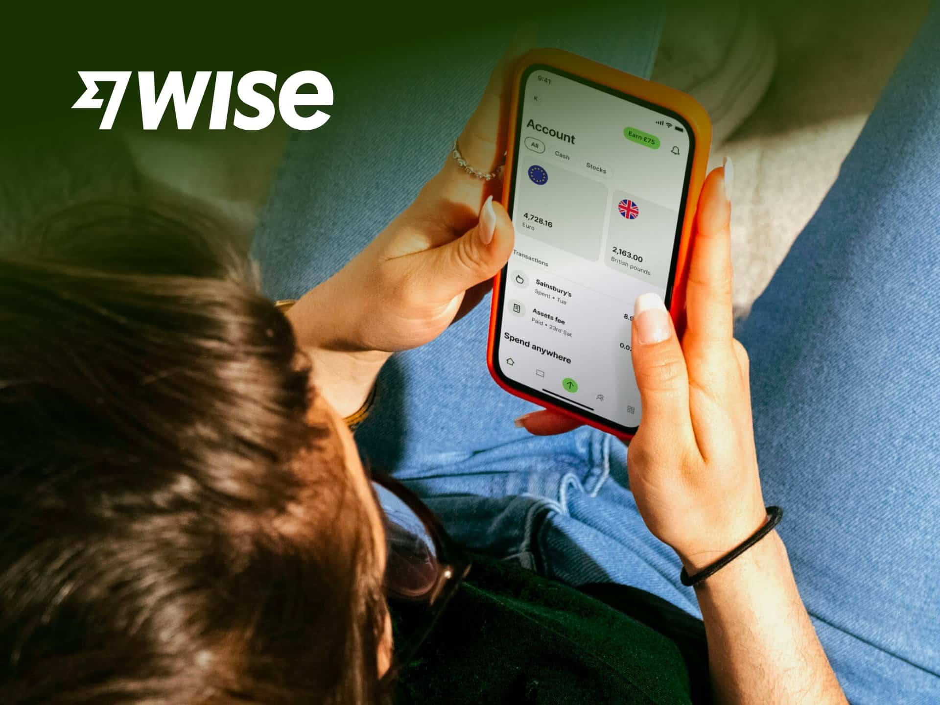 Person using the Wise app on a smartphone, showcasing financial management features, while seated casually.