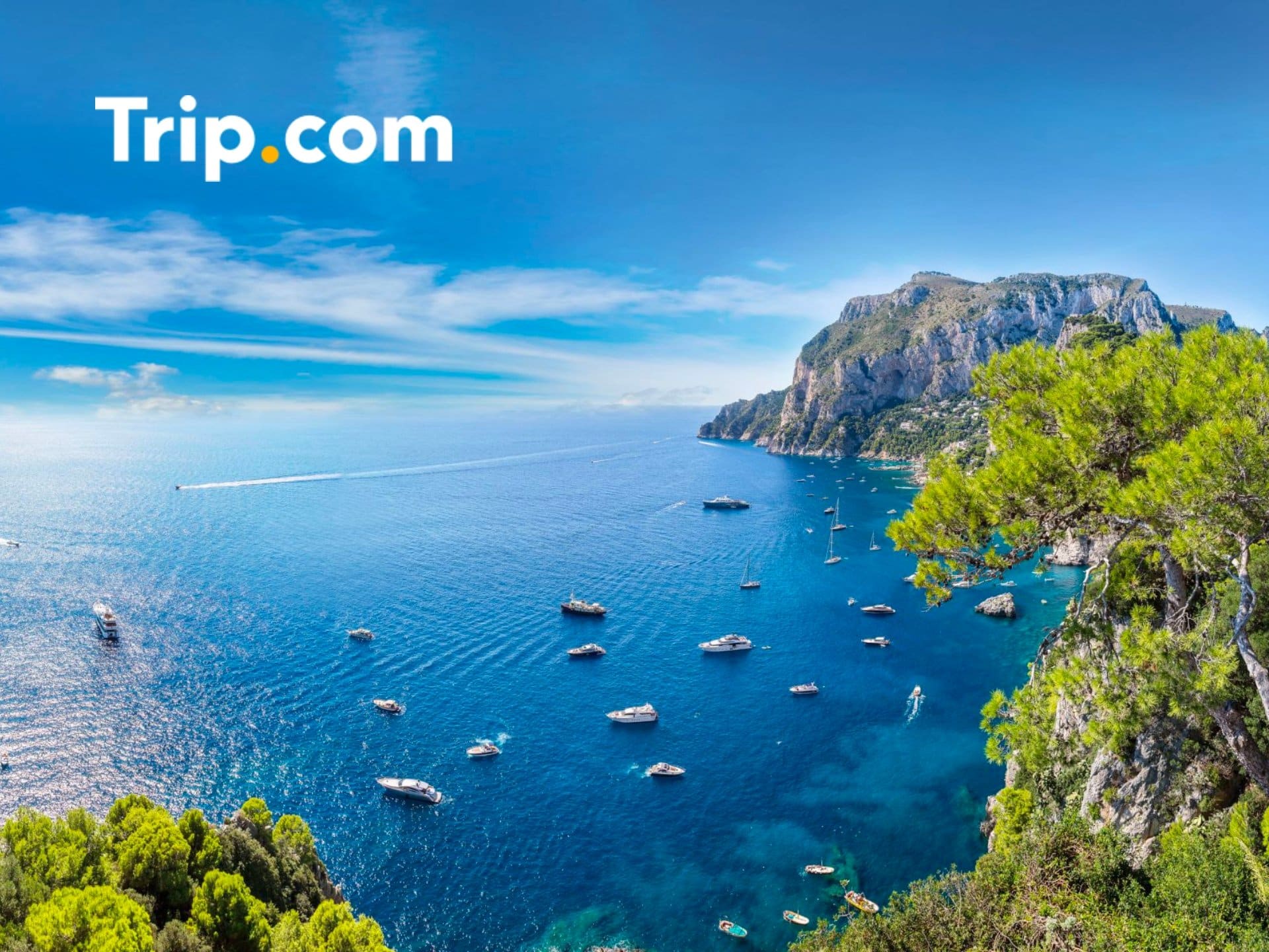 Scenic View Of The Mediterranean Coastline With Clear Blue Waters, Boats Sailing, And Lush Greenery, Featuring The Trip.com Logo.