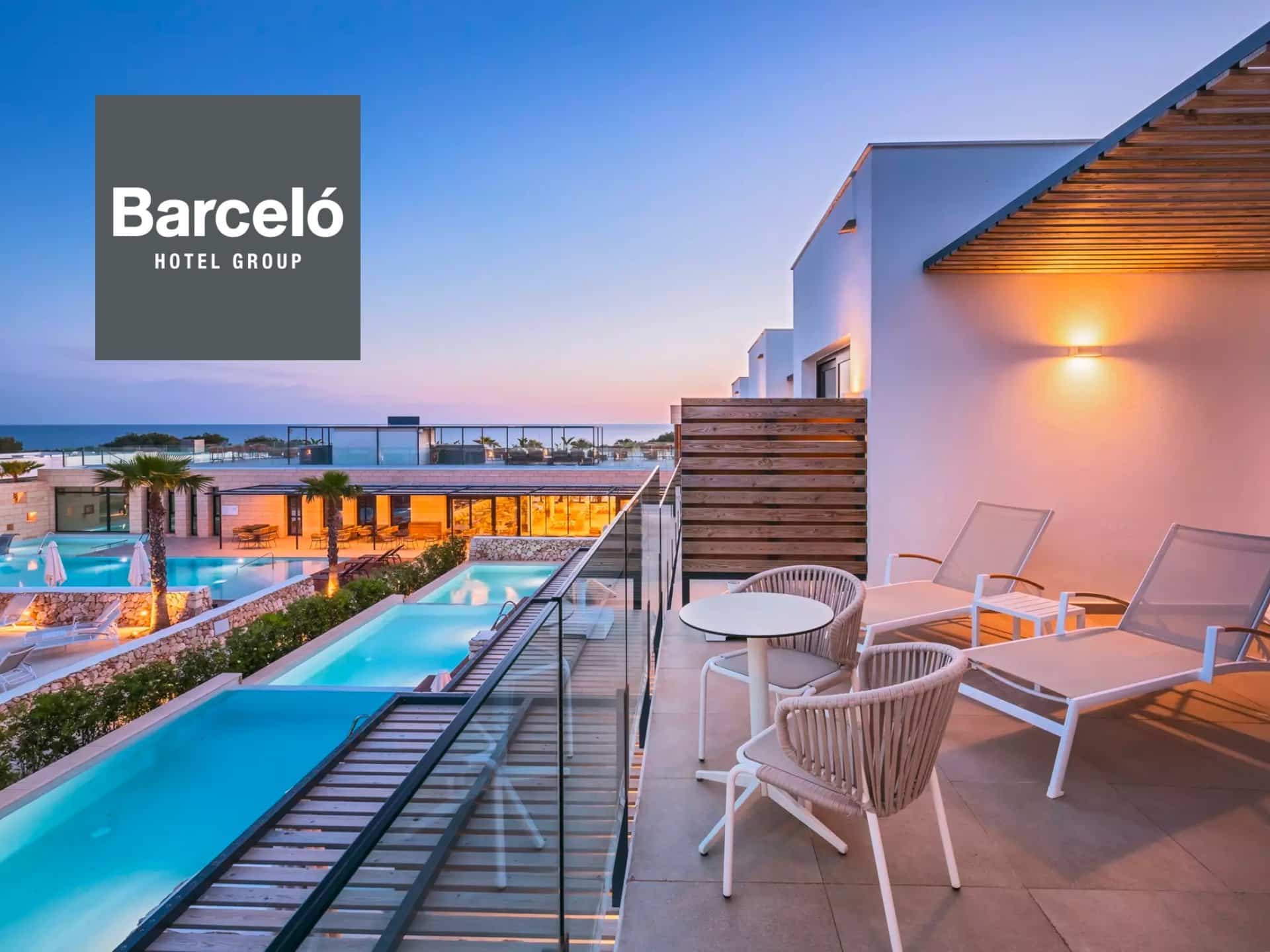 Balcony View Of A Luxury Hotel At Barceló, Featuring A Serene Pool Area And Modern Outdoor Furniture, With A Vibrant Sunset In The Background.