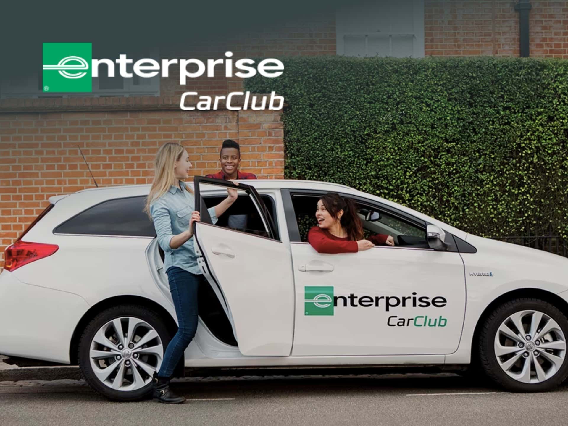 Two people interacting beside a white Enterprise CarClub vehicle, showcasing the car-sharing service's branding in a residential setting.