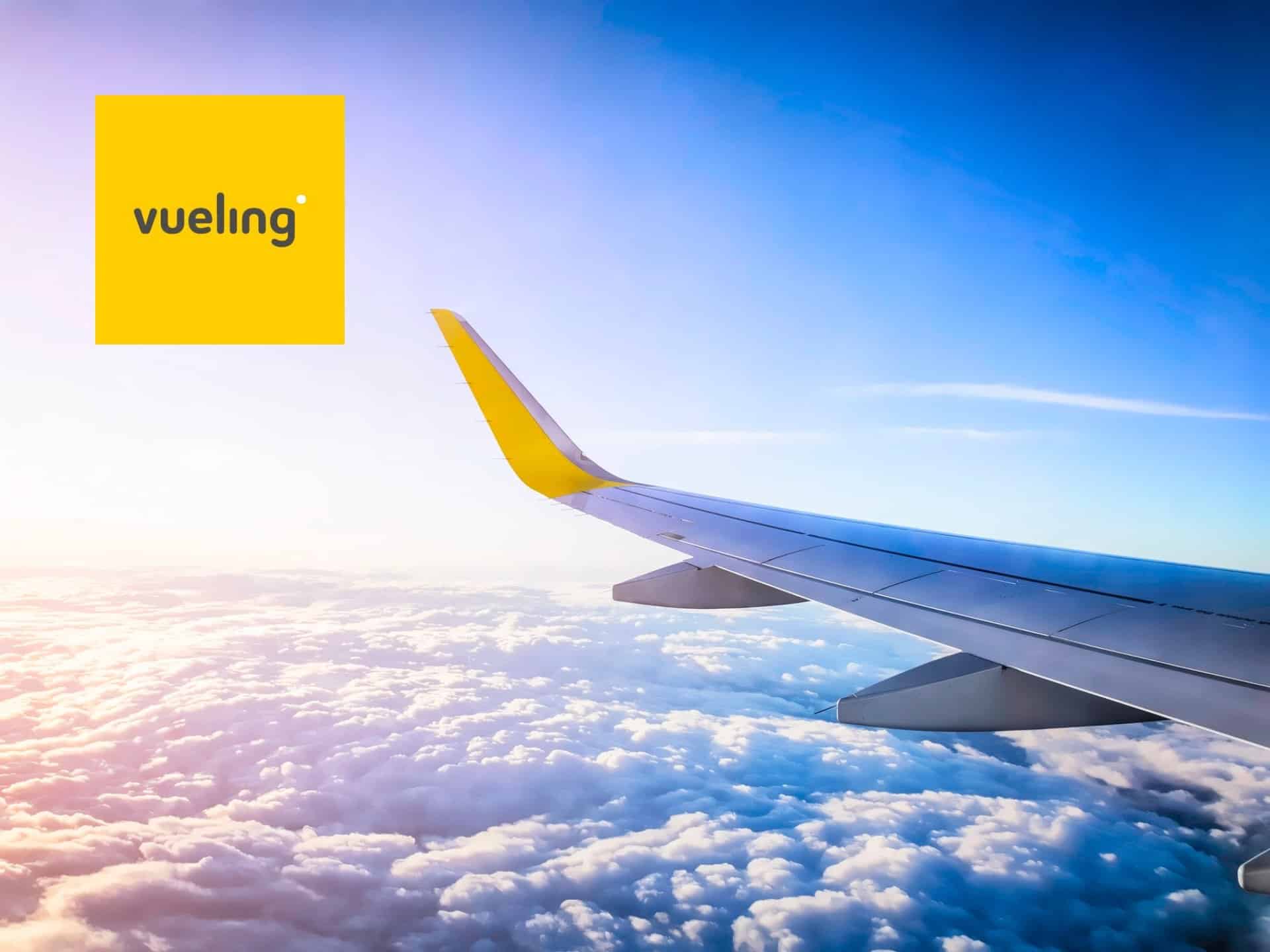 Aerial View From An Airplane Window Showing Clouds And Blue Sky With The Vueling Airlines Logo In The Corner.