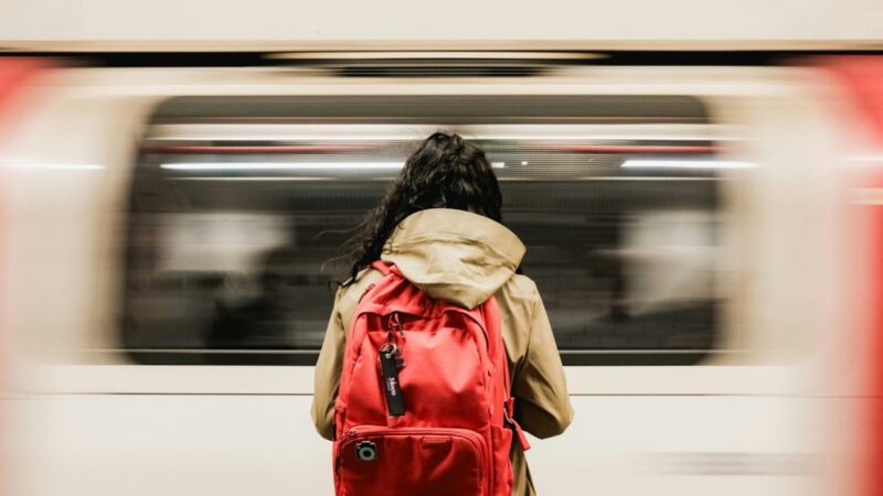 A person with a red backpack waiting as a train speeds past in the London Underground.